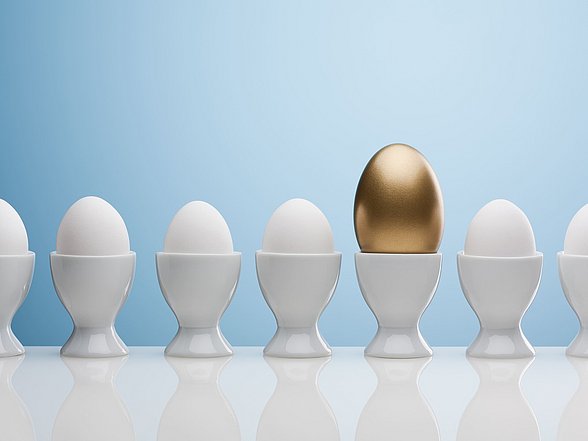 Mehrere Eier in Eierbechern in einer Reihe. Ein Ei ist Gold.
