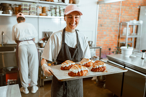 Praktikantin hält Backblech mit Croissants in den Händen