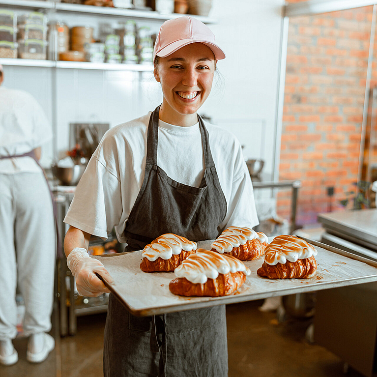 Praktikantin hält Backblech mit Croissants in den Händen.