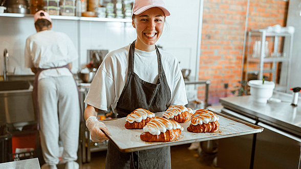 © dima_sidelnikov_istock Praktikantin hält Backblech mit Croissants in den Händen