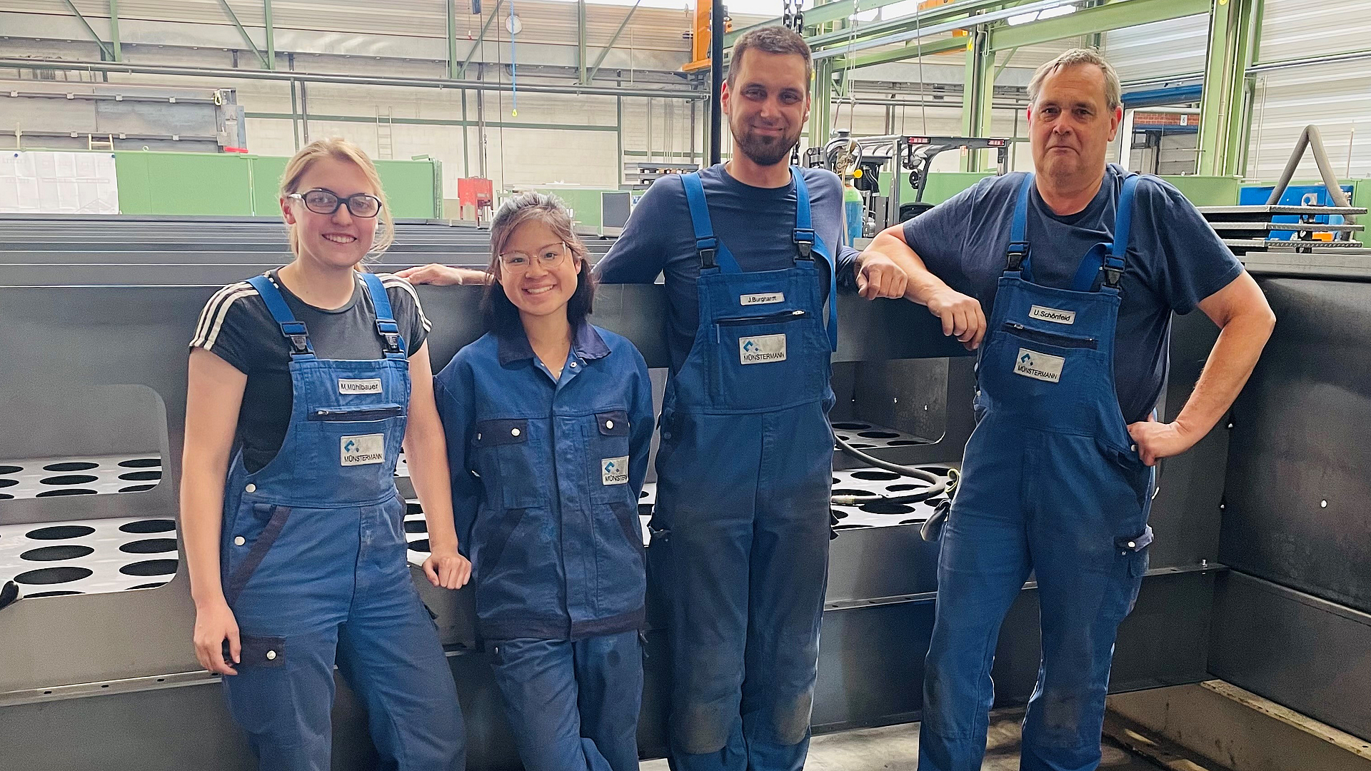 Zwei Frauen und zwei Männer stehen vor einer Anlage, gekleidet in blaue Arbeitskleidung.