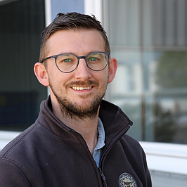 ©KOFA Portrait Christian Herrmann. Ein dunkelhaariger Mann Mitte 30 mit Brille und einem freundlichen Lächeln.
