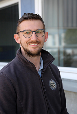 Portrait Christian Herrmann. Ein dunkelhaariger Mann Mitte 30 mit Brille und einem freundlichen Lächeln.