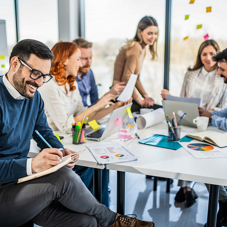 Sechs Personen sitzen in einem Meeting am Tisch 