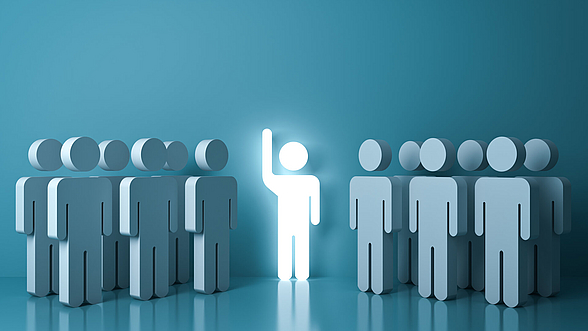 © masterzphotois-istock Leuchtendes Männchen steht inmitten von anderen Männchen und hebt die Hand