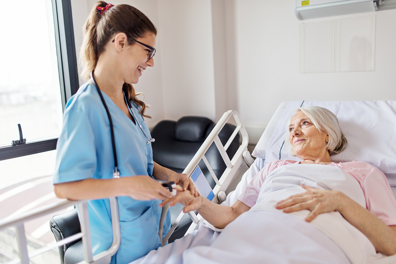 Krankenpflegerin versorgt ältere Dame im Krankenbett