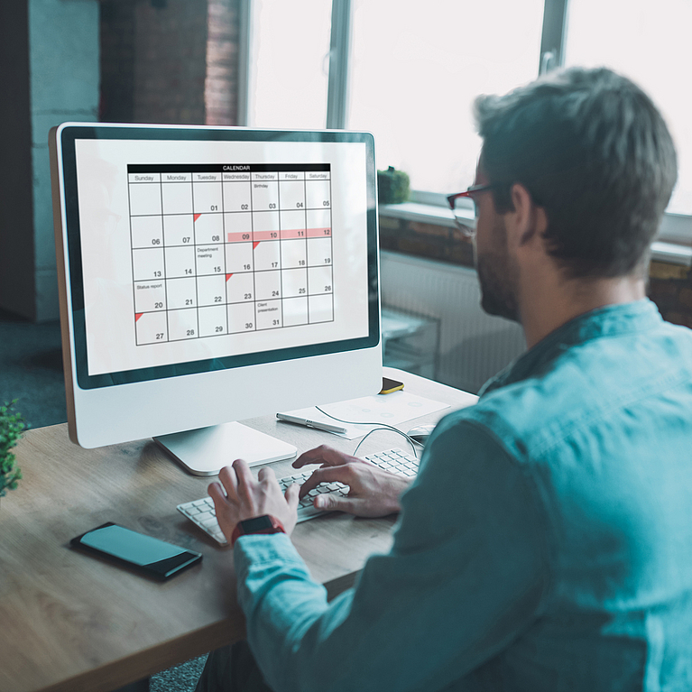 Mann sitzt am PC und hat einen Kalender geöffnet