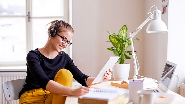 © Halfpoint– istock.com Junge Frau sitzt am Schreibtisch und nimmt an einem digitalen Lernformat teil