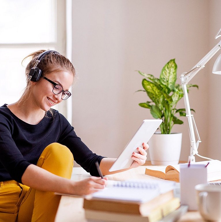 Junge Frau sitzt am Schreibtisch und nimmt an einem digitalen Lernformat teil