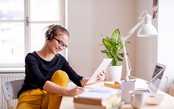 Junge Frau sitzt am Schreibtisch und nimmt an einem digitalen Lernformat teil