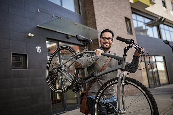 Ein Mann trägt lächelnd ein Fahrrad auf der Schulter.
