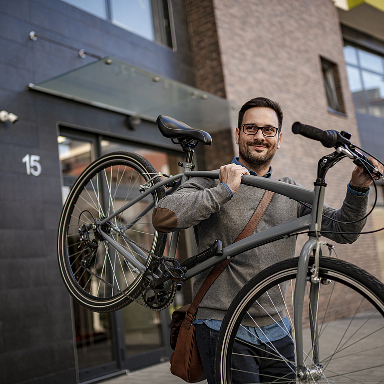 Ein Mann trägt lächelnd ein Fahrrad auf der Schulter.