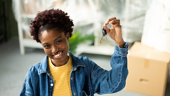 © RgStudio - iStock.com Frau hält lächelnd ihren neuen Wohnungsschlüssel in die Kamera.