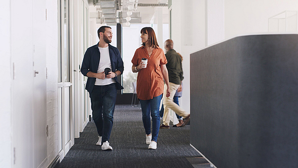 © shapecharge – istock.com  Zwei Mitarbeiter gehen über den Flur und unterhalten sich