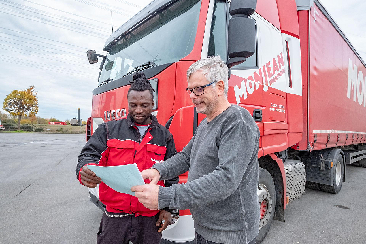 Älterer Mann mit Aufträgen in der Hand und dunkelhäutiger LKW-Fahrer