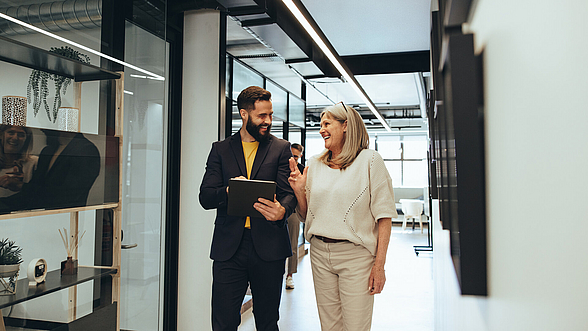 Ein junger Mann und eine mittelalte Frau unterhalten sich im Flur in einem Büro