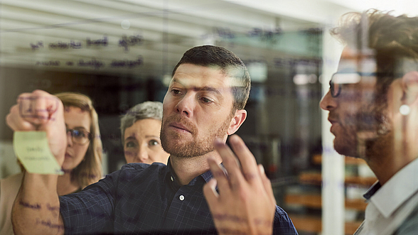 Mann klebt Post-it Zettel an eine Pinnwand aus Glas