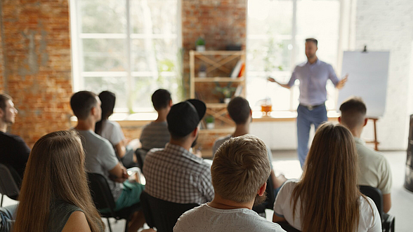 © master1305 -istock.com  Ein Mann steht vor einem Flipchart und hält einen Vortrag vor einer Gruppe