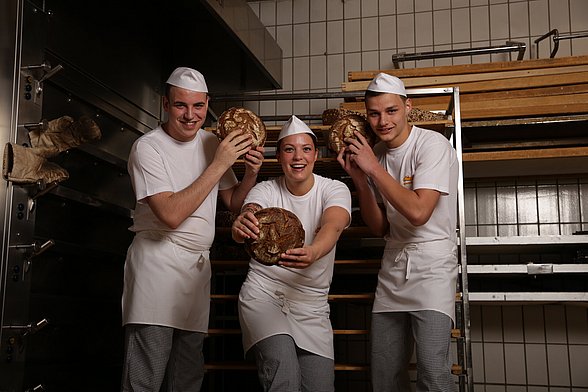 Drei Beschäftigte der Bäckerei Newzella posieren mit Brot in der Hand