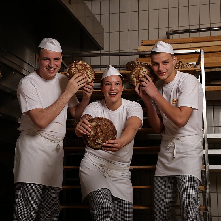 Drei Beschäftigte der Bäckerei Newzella posieren mit Brot in der Hand.