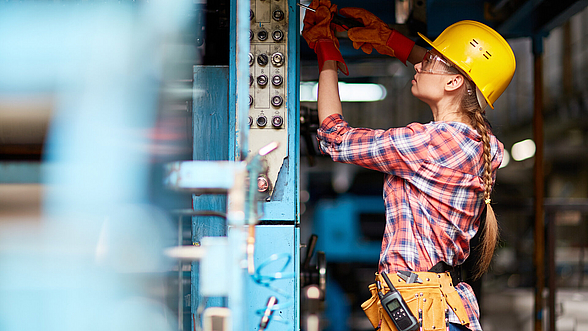 Facharbeiterin mit Schutzhelm justiert eine Industriemaschine