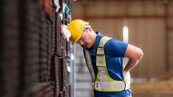Ein Mann mit schmerzverzerrtem Gesicht in Schutzausrüstung hält die Hand an den unteren Rücken.