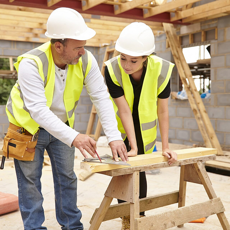 Ausbilder und Auszubildende an einem Holzstück in der Werkstatt