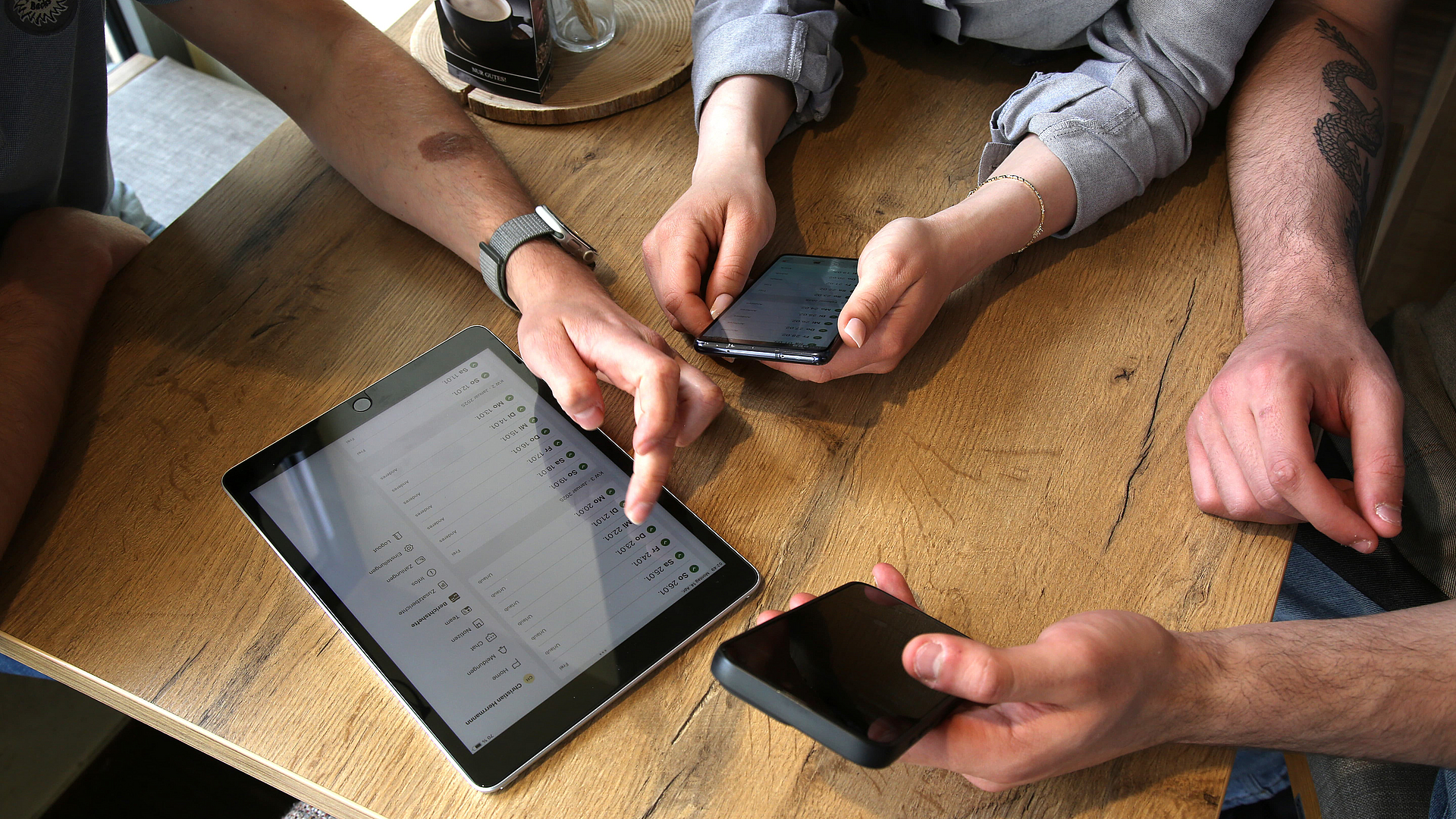 ©KOFA Azubis und Ausbilder beim Gespräch. Man sieht die technischen Geräte Tablet und Smartphone, über die das Berichtsheft gepflegt wird.