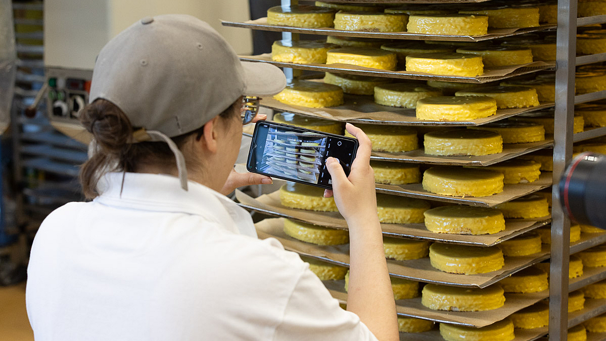 ©KOFA Auszubildende macht mit einem Smartphone ein Foto von vorbereiteten Teigwaren für ihr Berichtsheft.