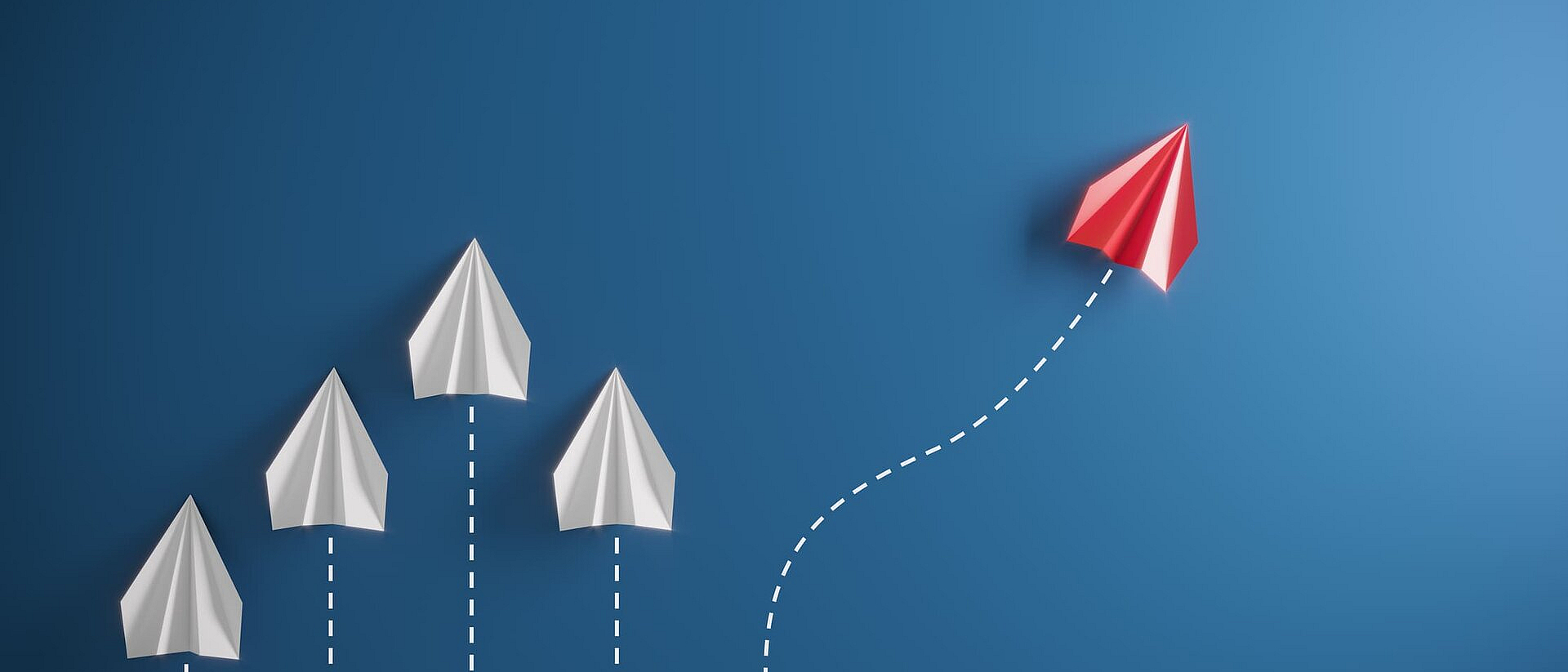 Vier weiße und ein roter Papierflieger auf blauem Hintergrund