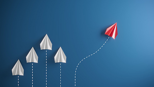 Vier weiße und ein roter Papierflieger auf blauem Hintergrund