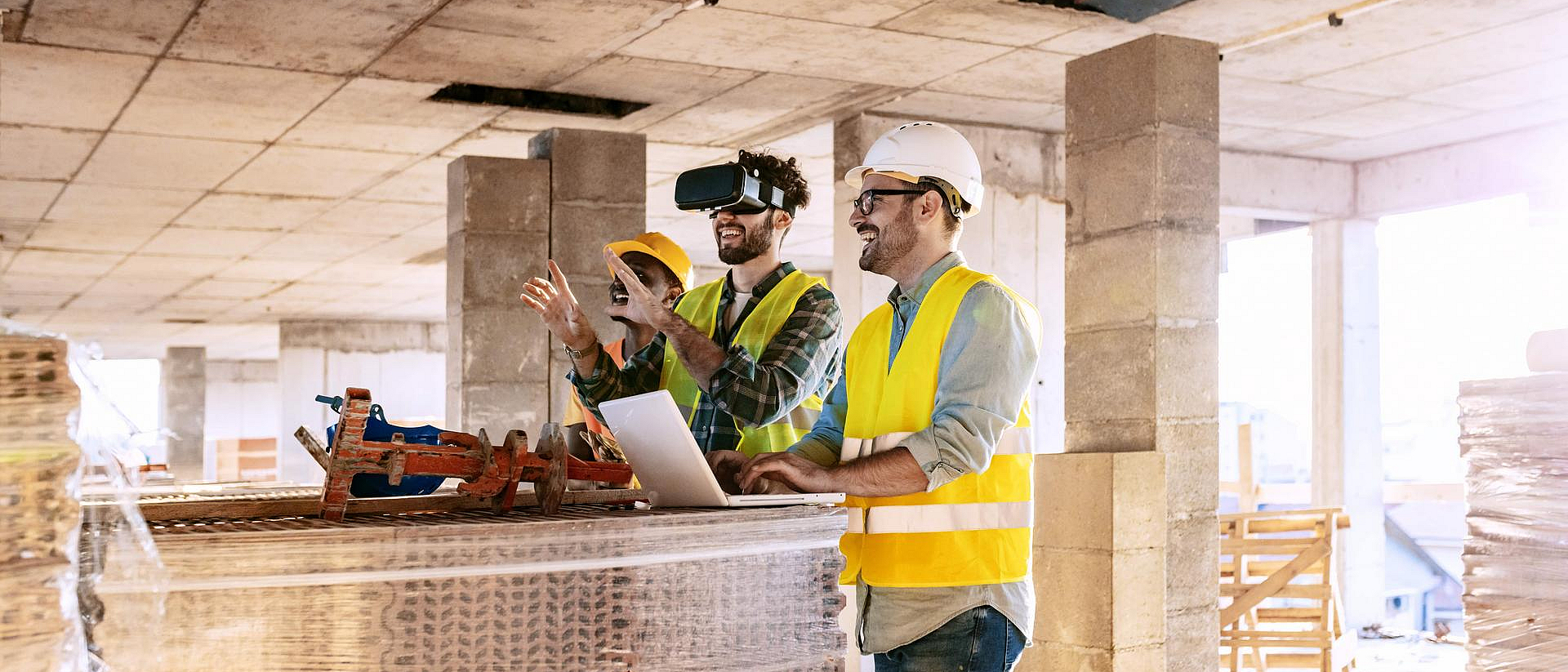 Drei Männer in gelben Warnwesten sehen sich in einem Rohbau die Zukunft mit VR-Brillen an