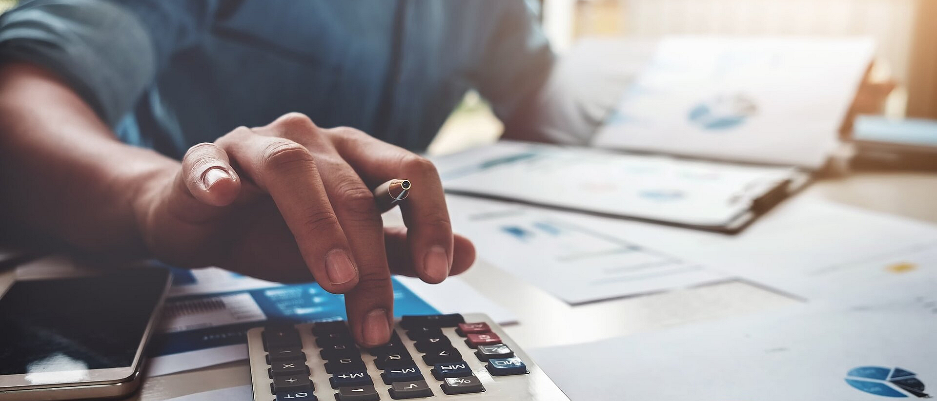 Mann in Jeanshemd an einem Schreibtisch bei einer Kalkulation