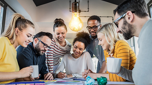 © scyther5 – istock.com Junge Menschen sitzen an einem Tisch und arbeiten zusammen