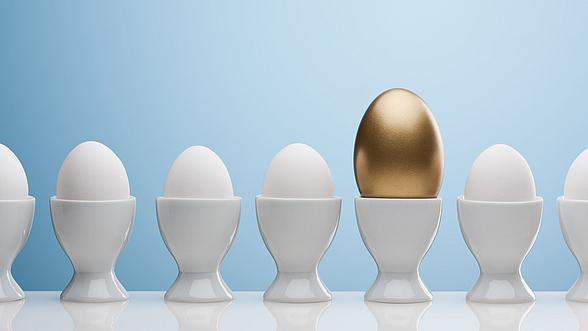 Mehrere Eier in Eierbechern in einer Reihe. Ein Ei ist Gold.