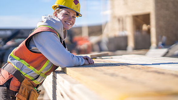 Junge Frau auf einer Baustelle mit Helm und Sicherheitsweste an.