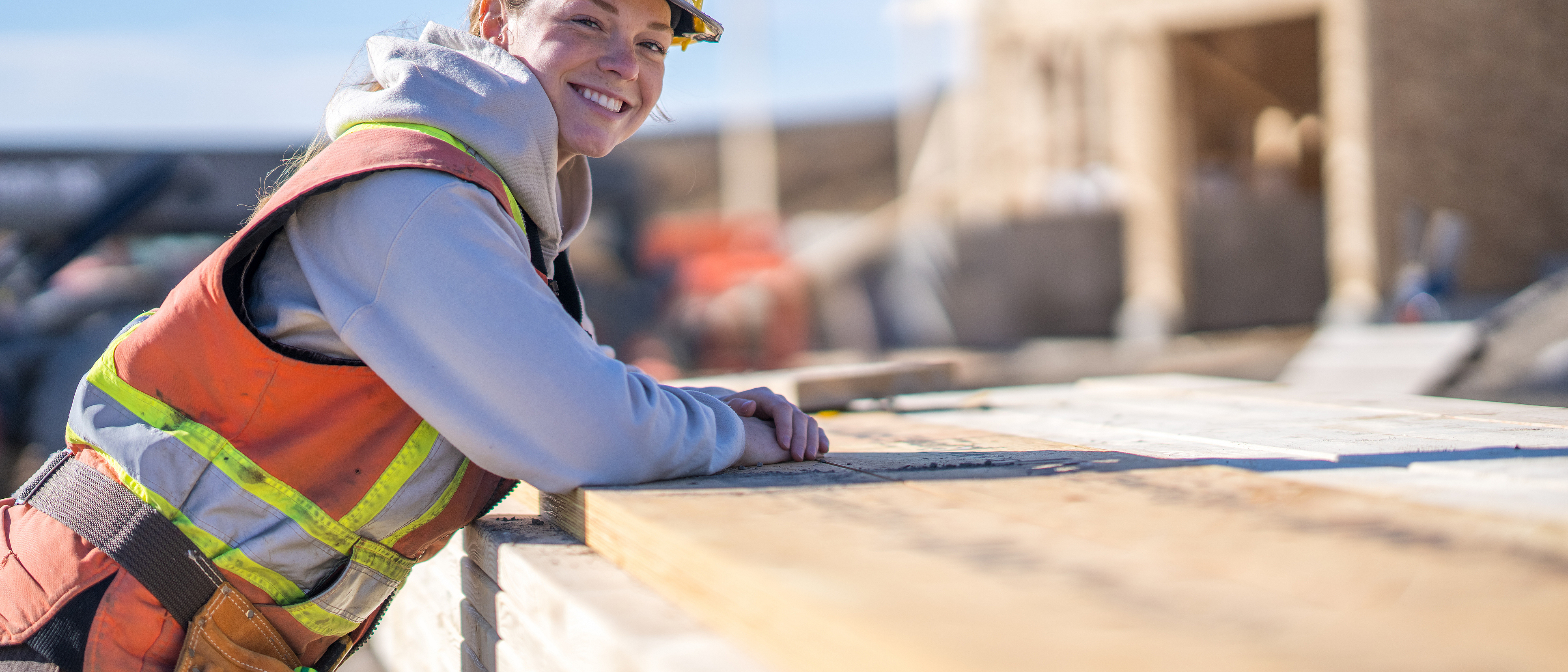 Eine Handwerkerin stützt sich auf einen Stapel Bretter.