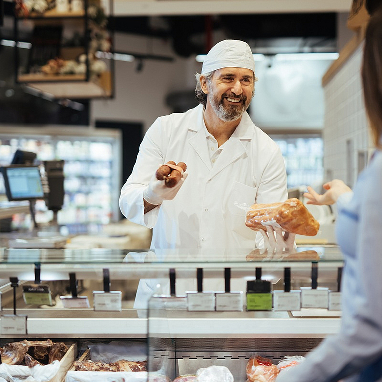 Mann bietet Kundin an der Theke eines SupermarktsFleischwaren an
