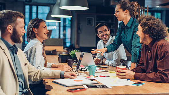 Fünft Personen sitzen am einem Tisch und diskutieren miteinander