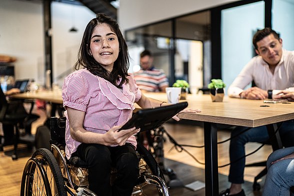 Porträt einer behinderten jungen Frau, die ein digitales Tablet bei der Arbeit benutzt