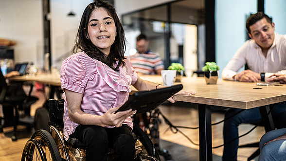 Porträt einer behinderten jungen Frau, die ein digitales Tablet bei der Arbeit benutzt