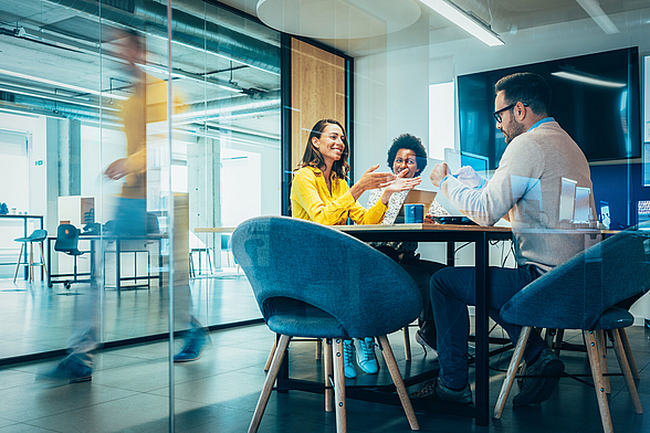 Drei Personen sitzen in einem Büro und besprechen sich