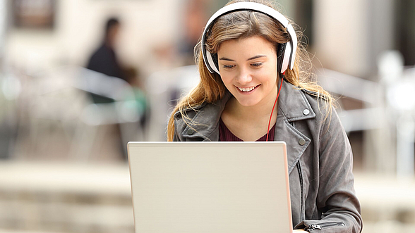 © AntonioGuillem– istock.com Junge Frau sitzt mit Laptop draußen im Freien