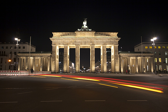 Brandenburger Tor mit schwarz-rot-goldenen Lichteffekten davor im Dunkeln.