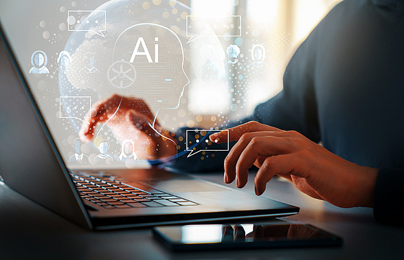 Person tippt am Computer über dessen Tastatur eine wolkige Darstellung Technologie abbildet.