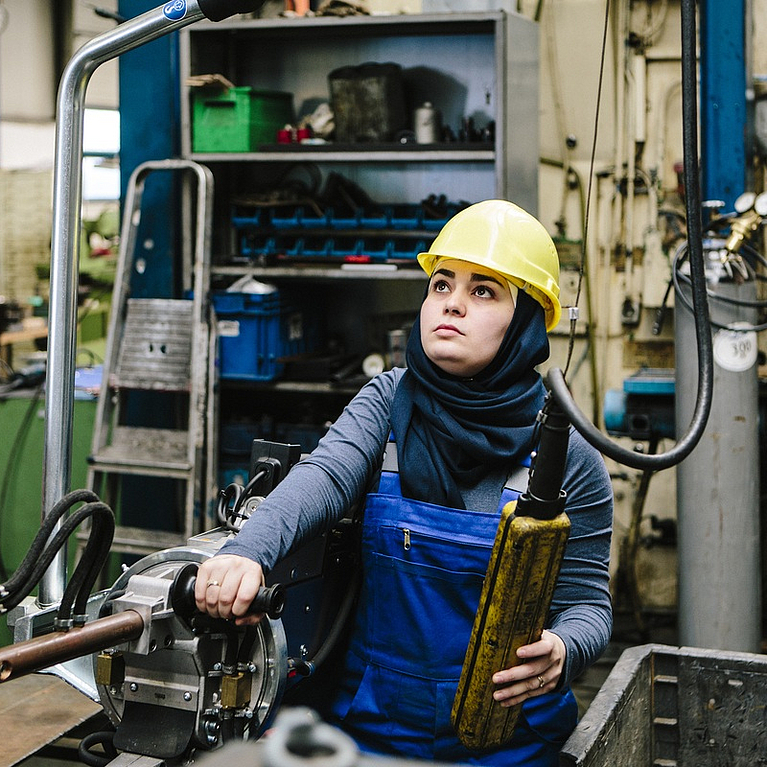 Junge Frau im Blaumann arbeitet in Fabrikhalle
