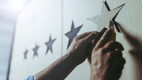 Zu sehen ist eine Hand, die einen Stern aufklebt. Insgesamt sind fünf Sterne zu sehen.