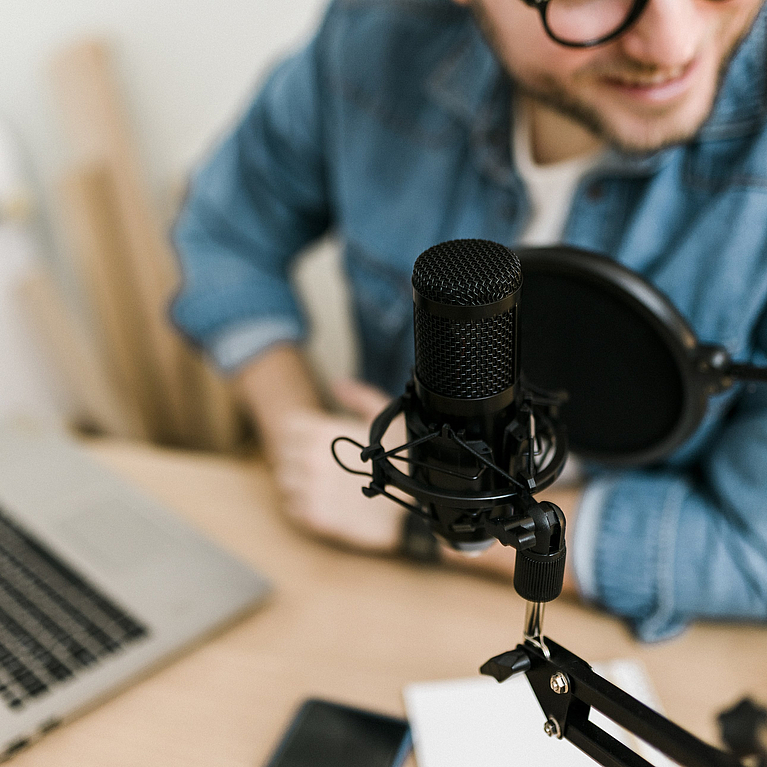 Nahaufnahme eines jungen lächelnden Mannes, der Podcast aufnimmt und Live-Streaming mit Mikrofon und Kopfhörern im Aufnahmestudio durchführt