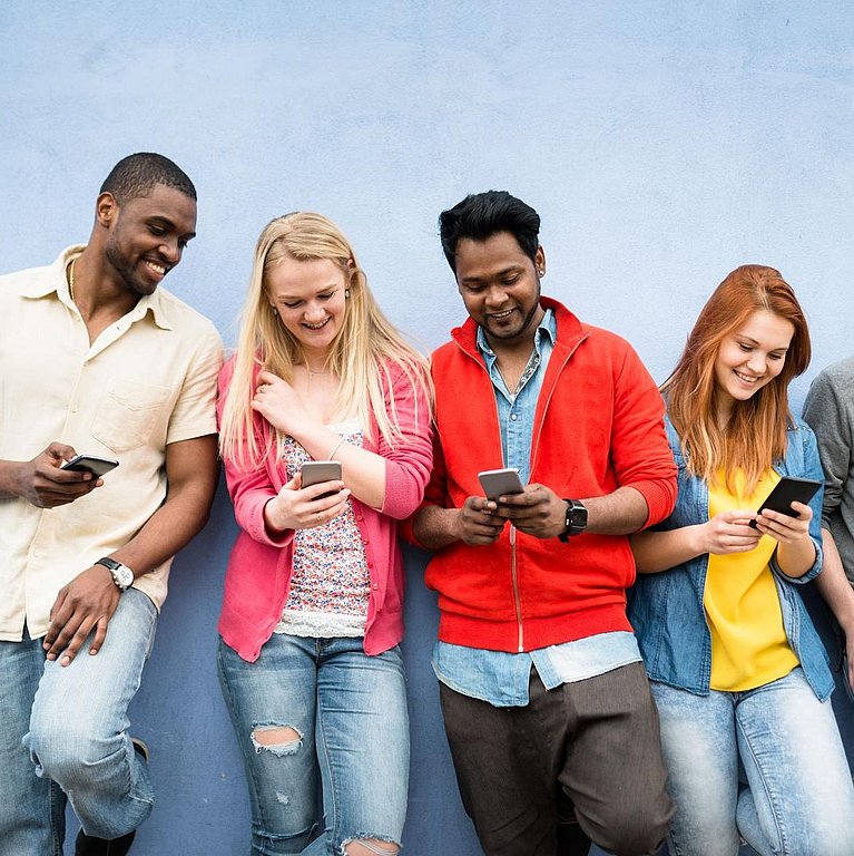 Fünf junge Menschen stehen mit Smartphones in der Hand an einer Wand gelehnt