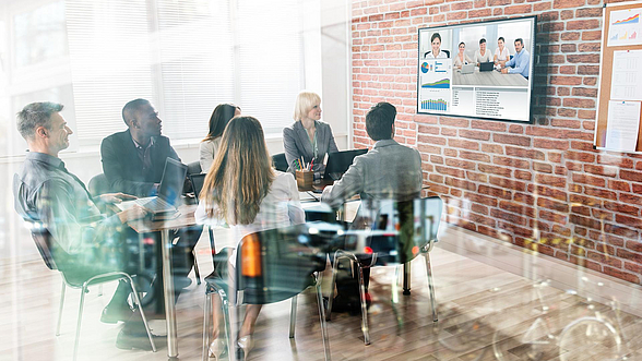 Menschen sitzen in einem Besprechungsraum und führen eine Videokonferenz